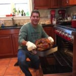 A man sitting in front of an oven holding a turkey.